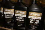 Bottle of Stan's Rolled Gold tubeless sealant beside a gravel bike wheel